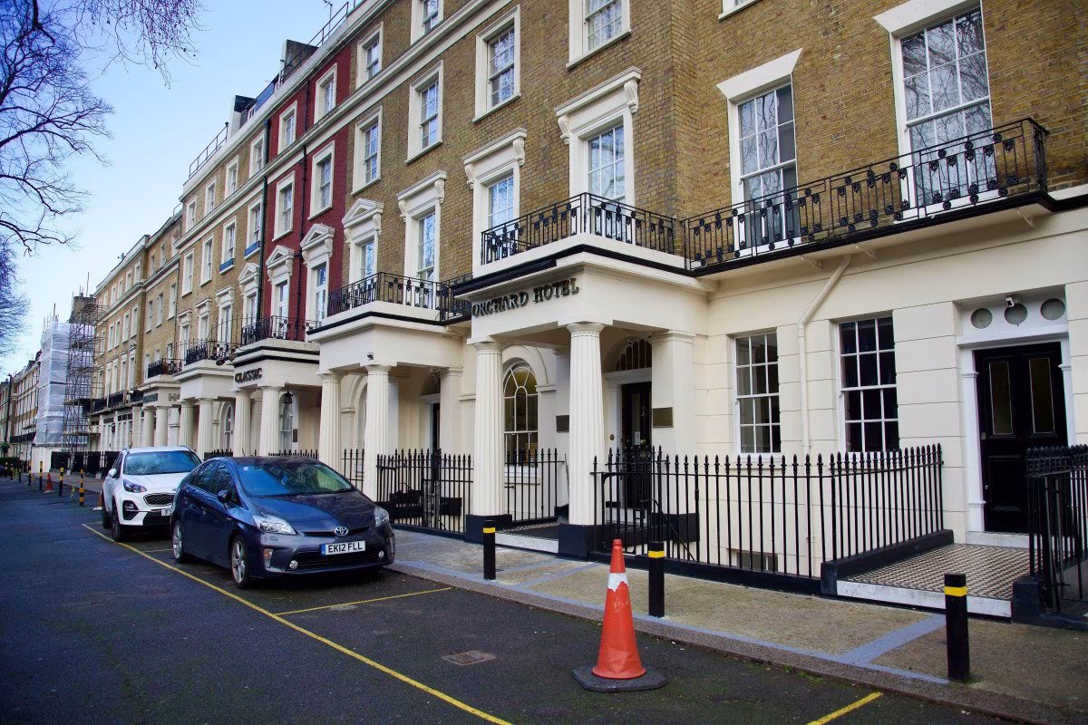 The Classic Hotel in London with a black fence and parked cars. from Stockmark.it