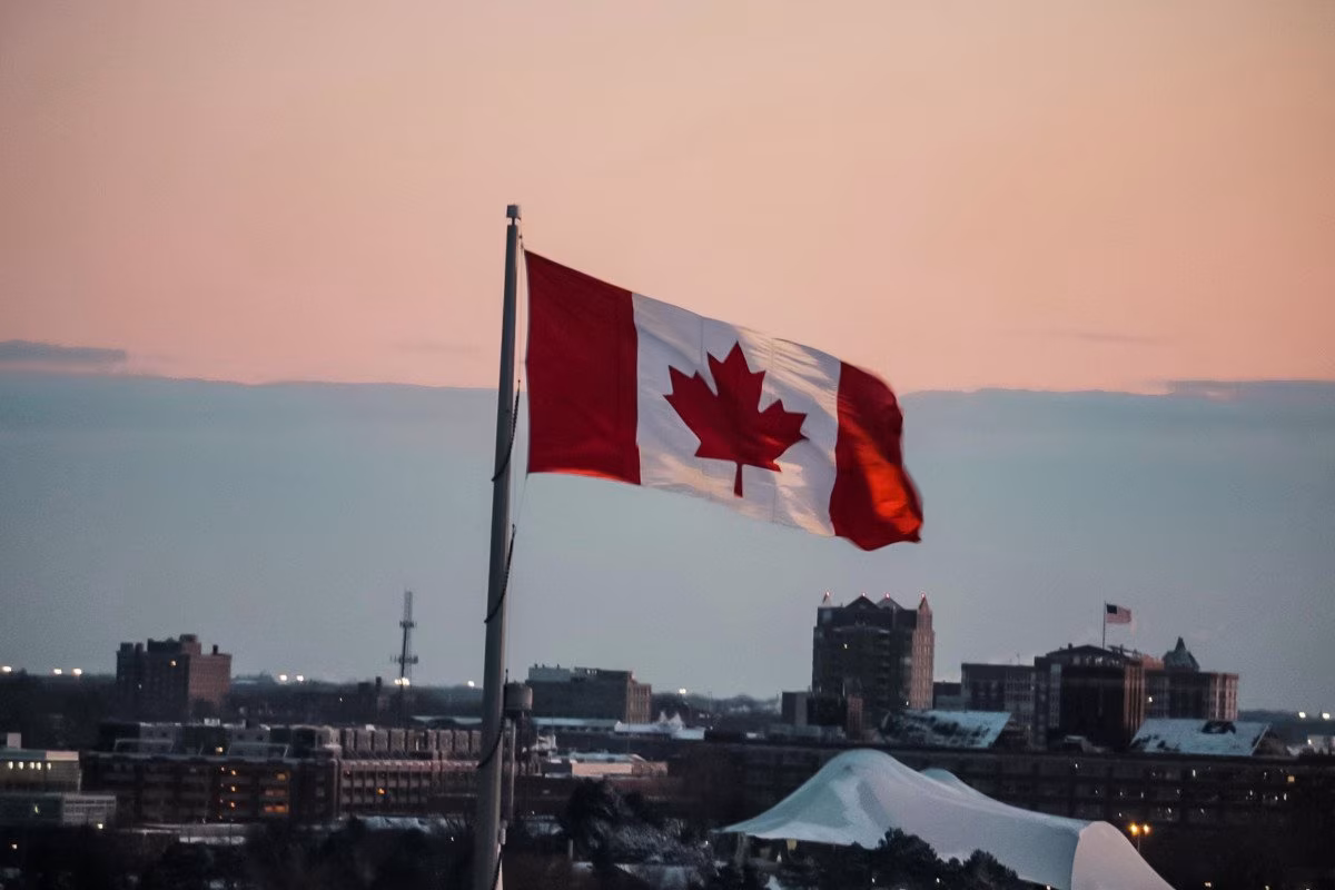 Canadian flag waving over city skyline at dusk, referencing net zero retreat. from Stockmark.it