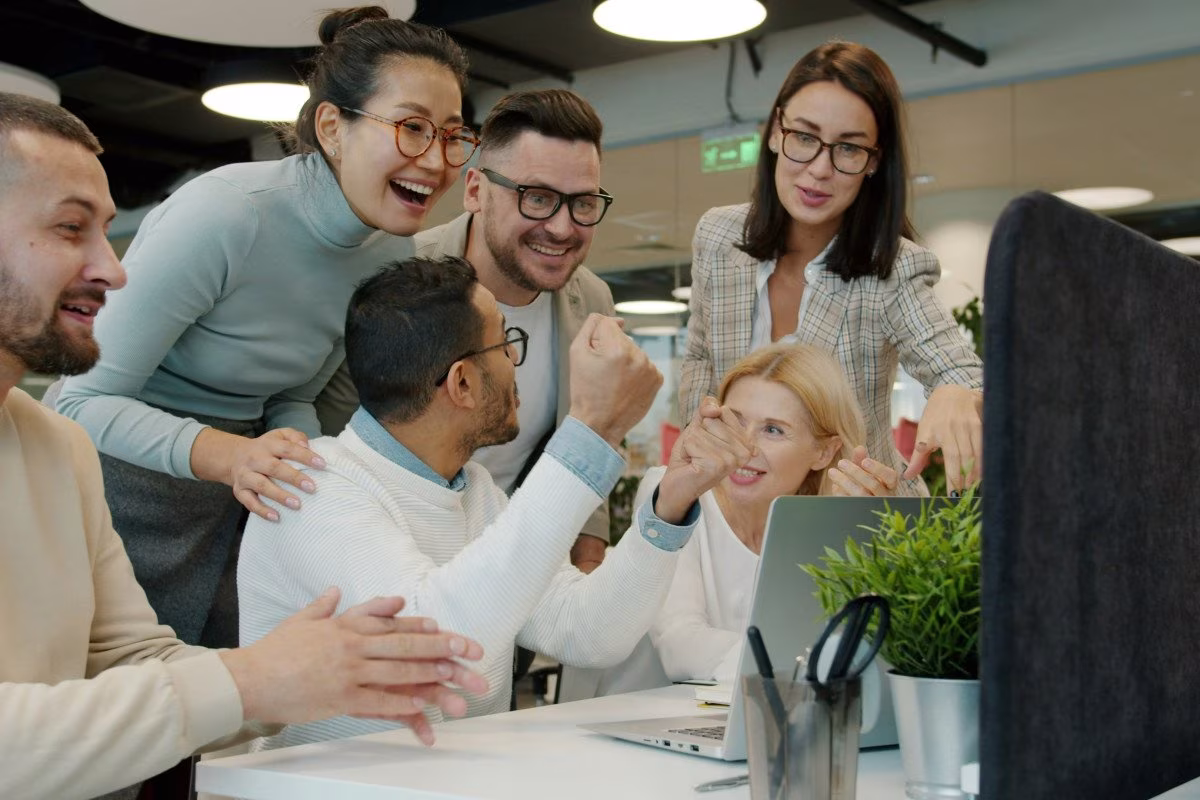 Diverse team celebrating success around a laptop, with Eventbrite and Vimeo mentioned. from Stockmark.it